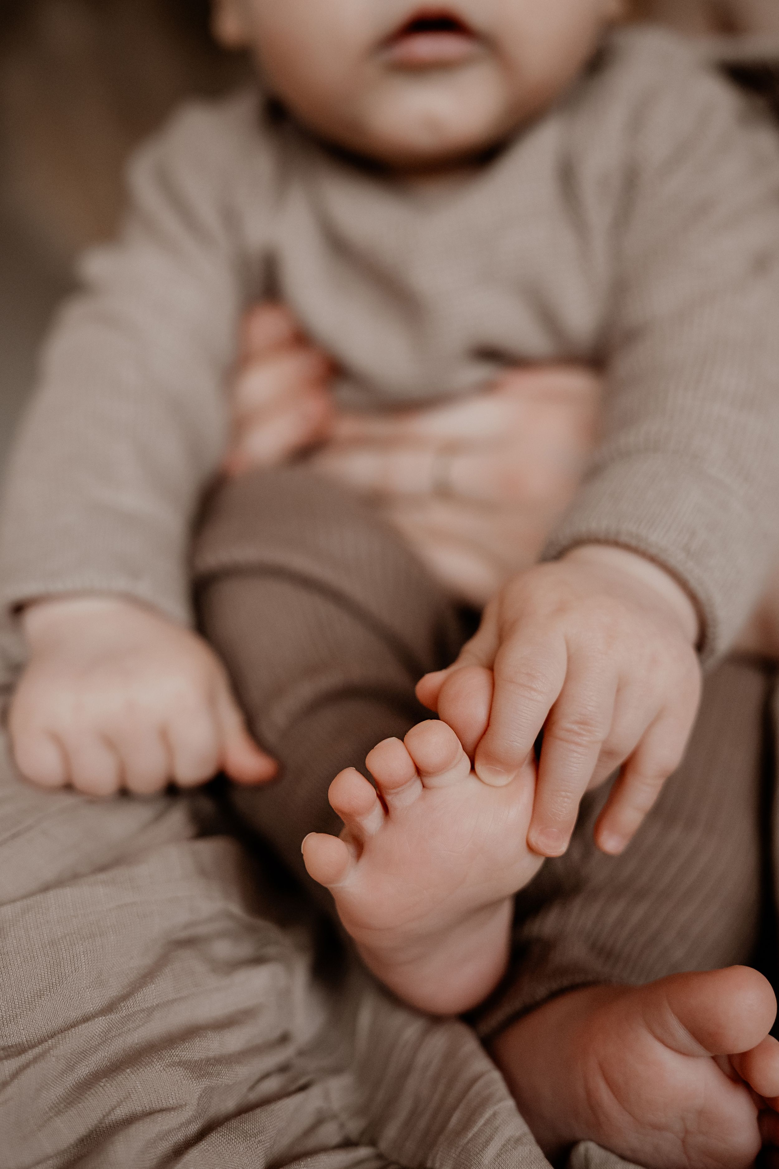 Close-up van kleine babyvoetjes en handjes op zacht beige geribd stof, waarbij de fijne details van de baby subtiel worden vastgelegd.