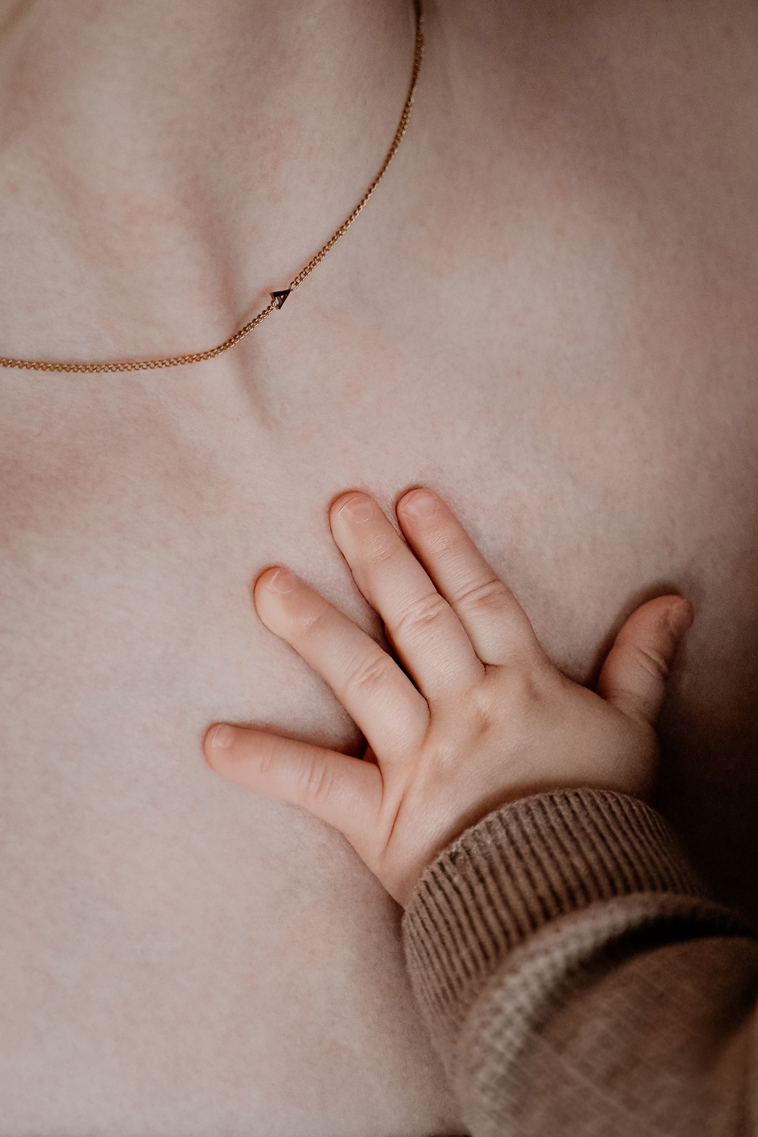 Close-up van een klein handje dat de borst aanraakt, met een delicate gouden ketting zichtbaar.