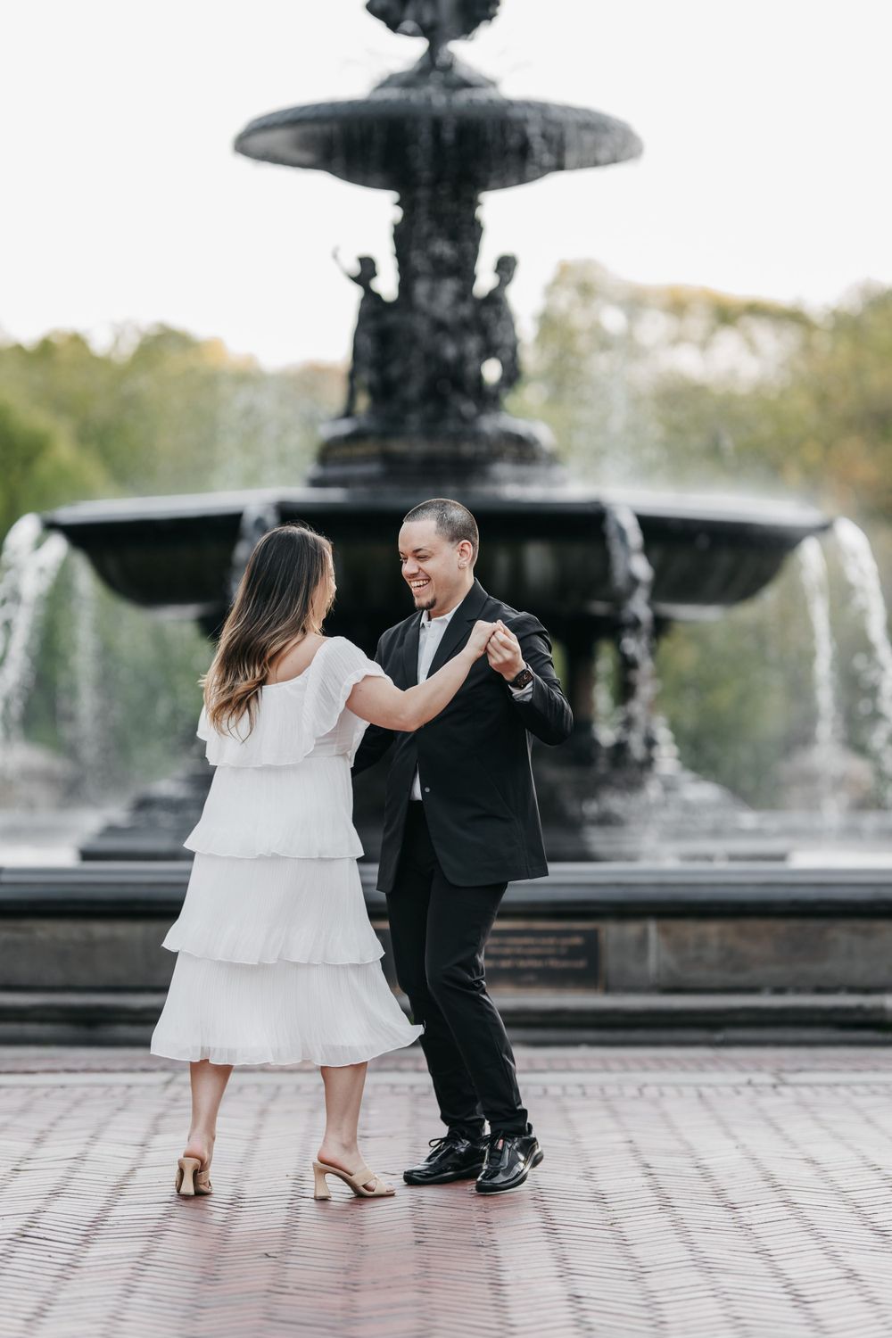 A couple dances together in front of Bethesda Fountain in Central Park, with the woman wearing a white tiered dress.