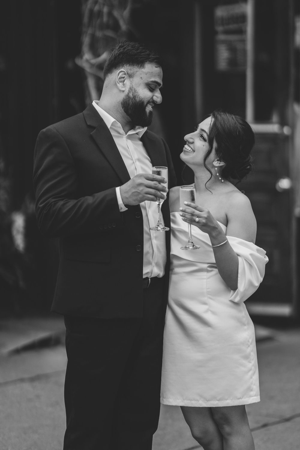 A romantic black and white shot of a couple sharing drinks and smiling at each other in formal attire.
