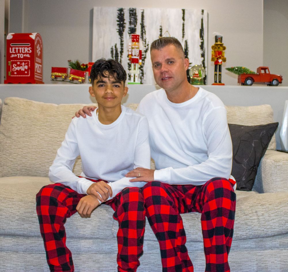 Boy and man in matching red plaid Christmas pajamas sitting together on a white couch.