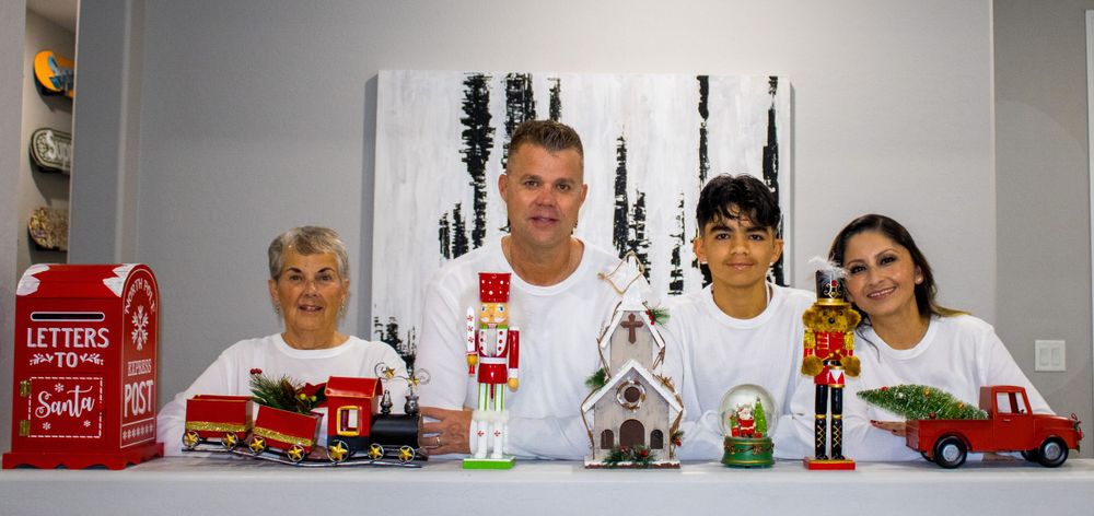 Family of four poses with Christmas decorations including nutcrackers and a gingerbread house on a white table.