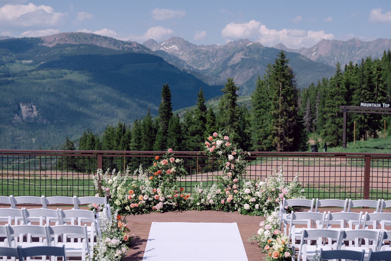 Mountain wedding ceremony setup with white chairs and floral arch against scenic backdrop.
