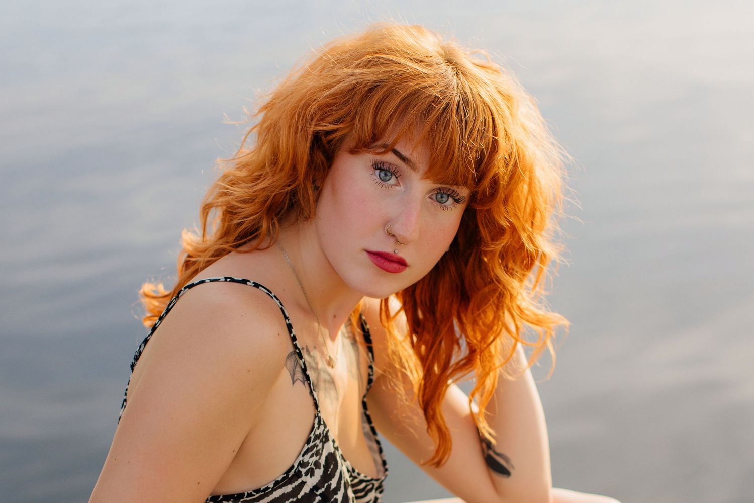 Vibrant red hair glows in warm sunlight against a serene water backdrop.