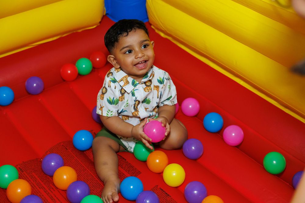 A toddler plays in a colorful ball pit with red, yellow and blue inflatable walls.