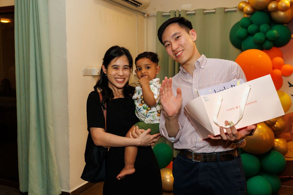 A family celebrates with colorful balloon decorations and presents at a festive party gathering.