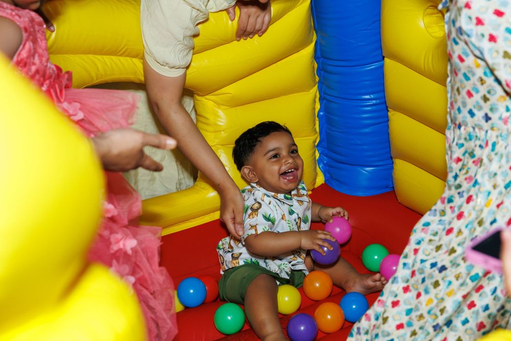 Child playing happily in colorful ball pit at indoor party venue.