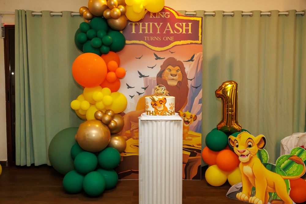 Lion King themed party setup with colorful balloon arch and decorative cake display.