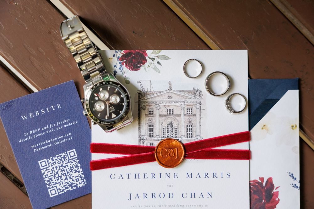 Wedding invitation with rings, watch and wax seal displayed on wooden surface.