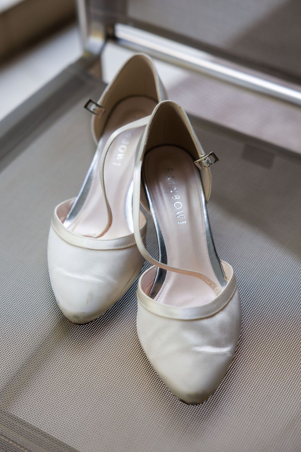 Elegant white satin bridal flats with small heels displayed on a grey surface.