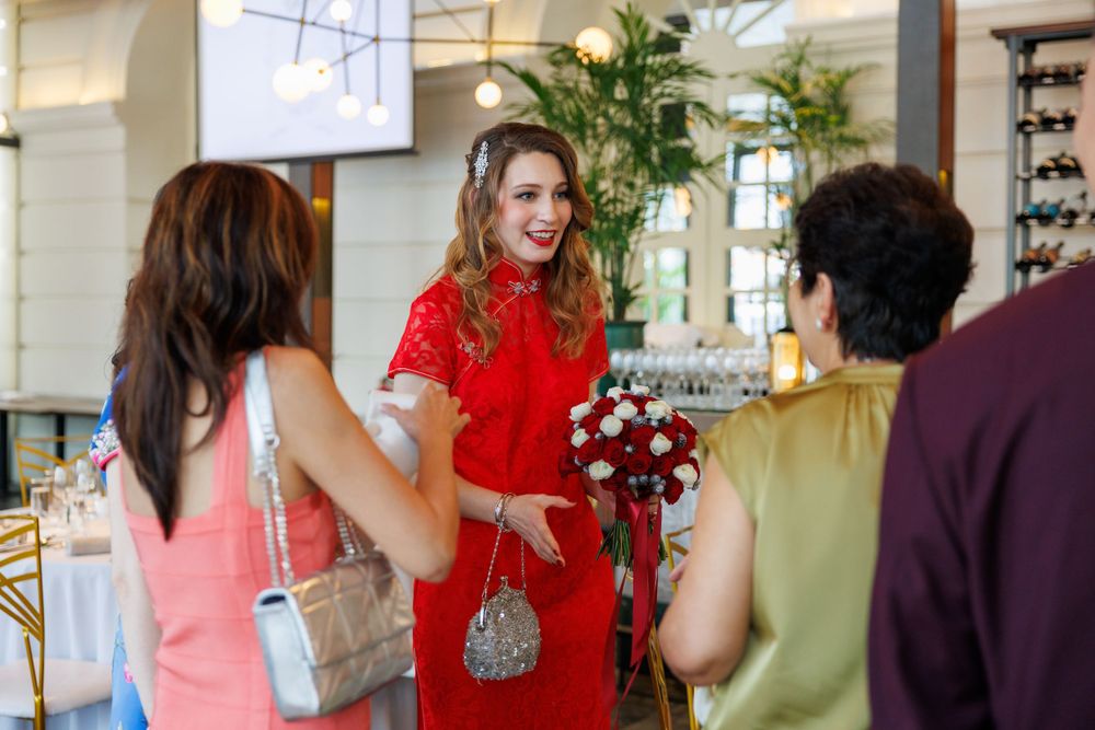 A group interacts at a celebration, with someone wearing a striking red dress holding a bouquet.