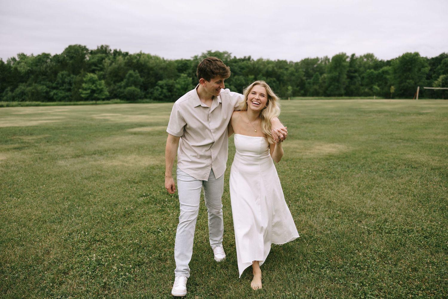 Couple in white and burgundy clothing embracing against white wall with natural lighting.