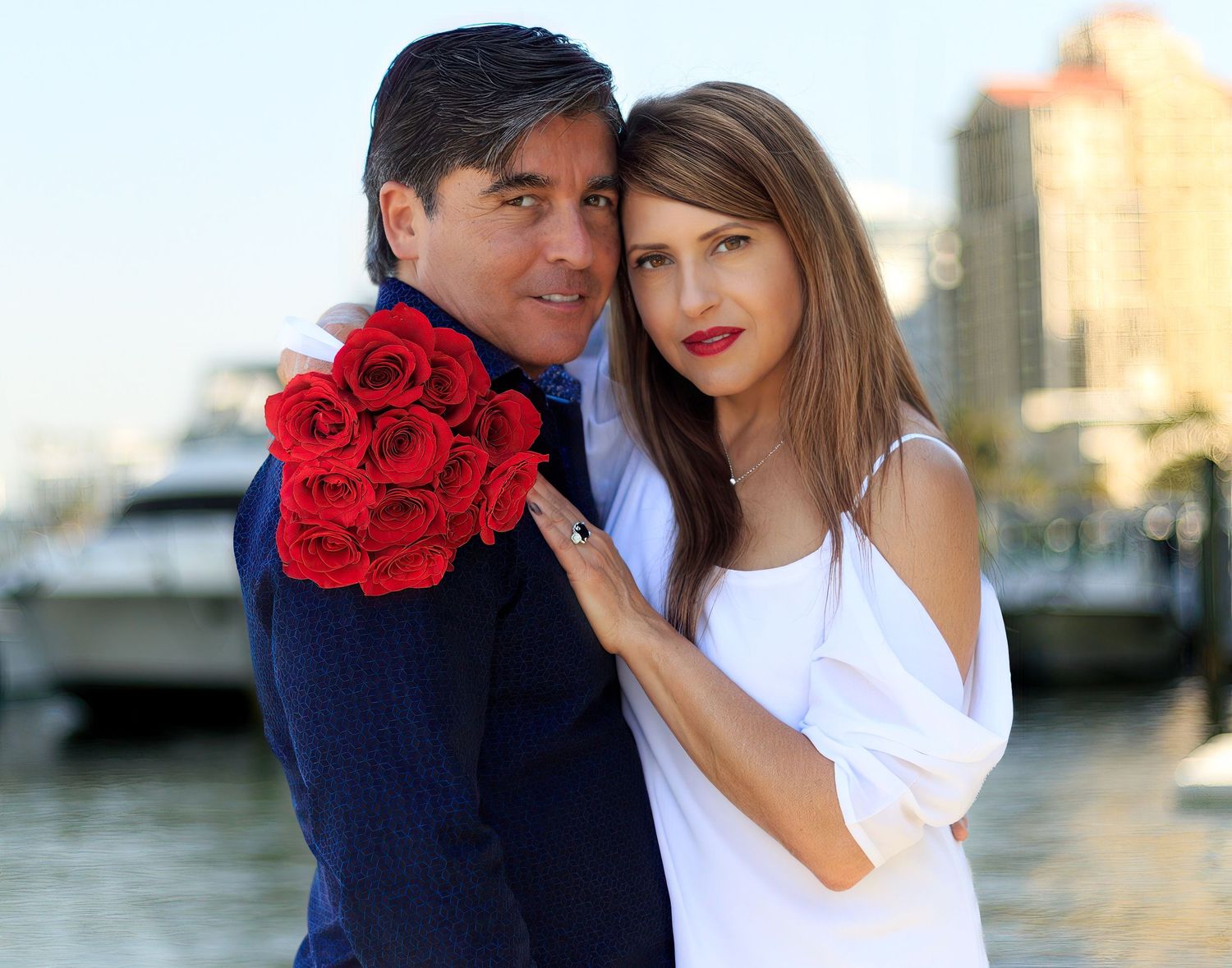 Romantic couple posing with red roses by waterfront at sunset.