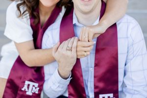 Close up shot showing hands with an engagement ring displayed against maroon Texas A&M University graduation stoles.