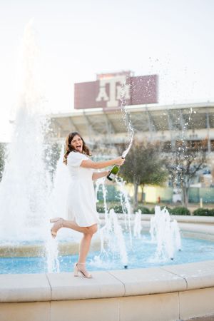 A celebratory scene with champagne being popped near a fountain at Texas A&M University campus.