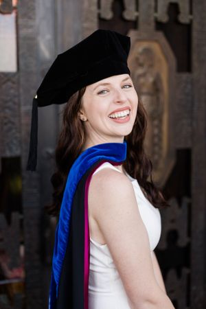 Graduate in black cap and blue-pink academic stole smiles while celebrating commencement at university ceremony.