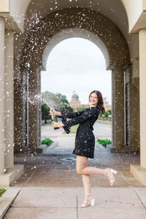 A woman in a polka dot dress poses playfully under an archway while glitter sparkles in the air around her.