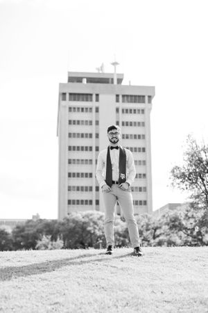 Black and white portrait of a casually dressed person standing on a hill with a tall apartment building in the background.