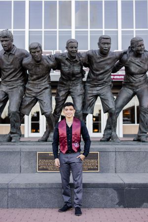 A person stands in front of a bronze statue group depicting football players engaged in a huddle formation.