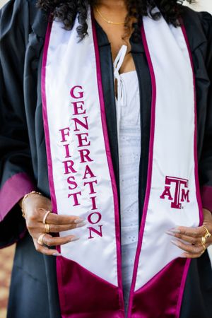A graduation stole with 'First Generation' text and Texas A&M logo in maroon on white fabric with maroon trim.