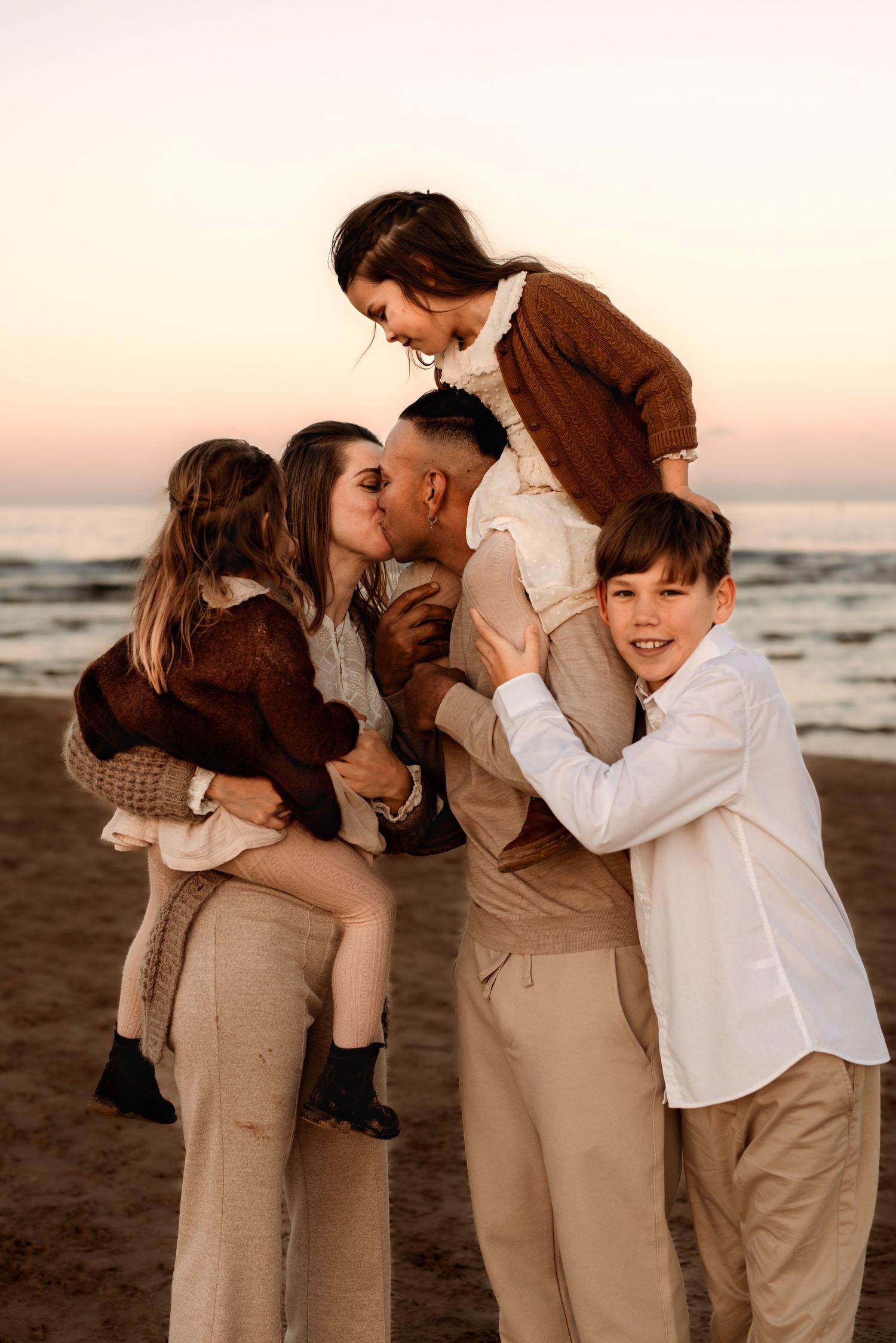 A family in coordinated brown and beige outfits in Denia share an intimate moment together on the beach at sunset. Denia photographer