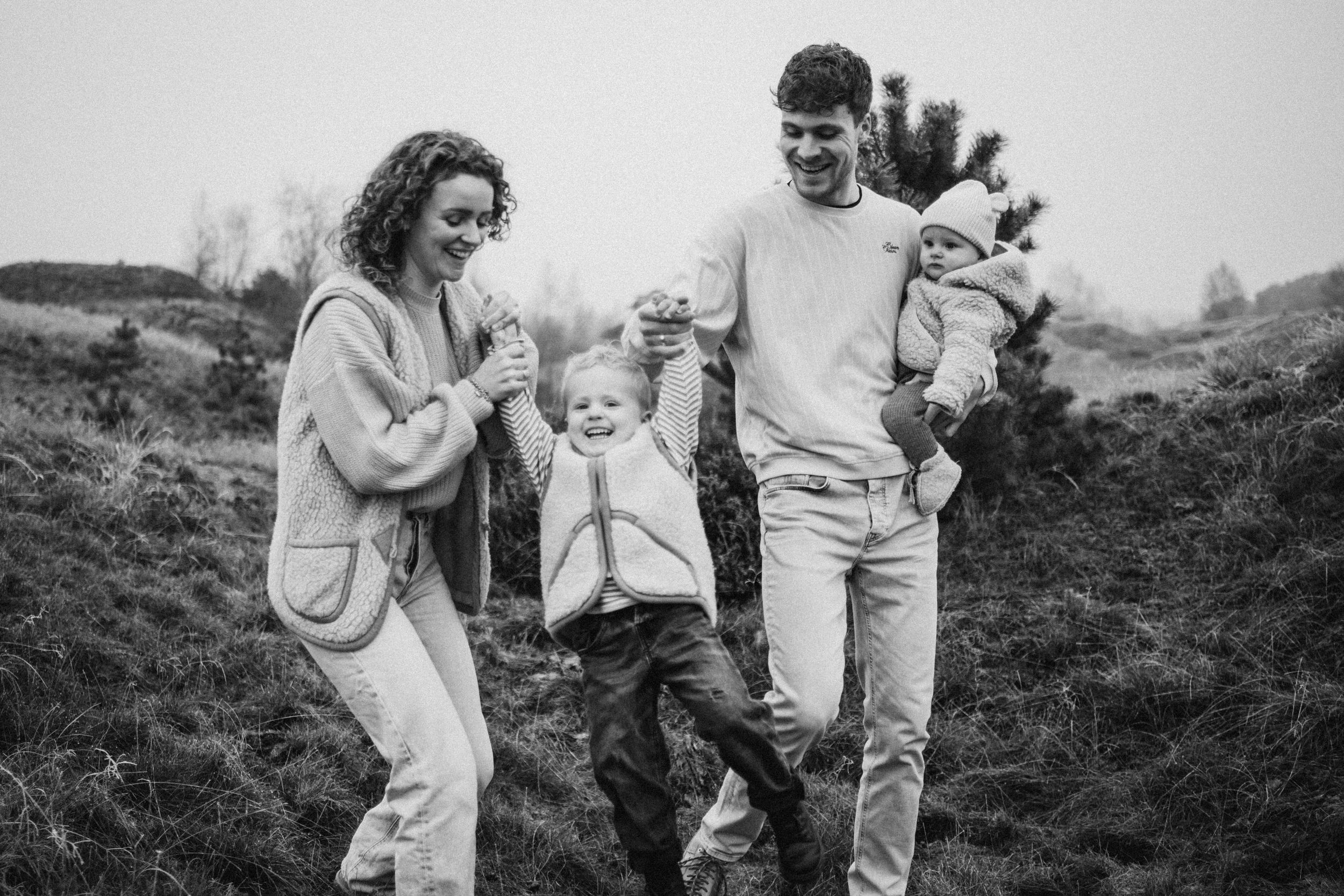 Family enjoying playful moments together on a hillside in black and white photography.