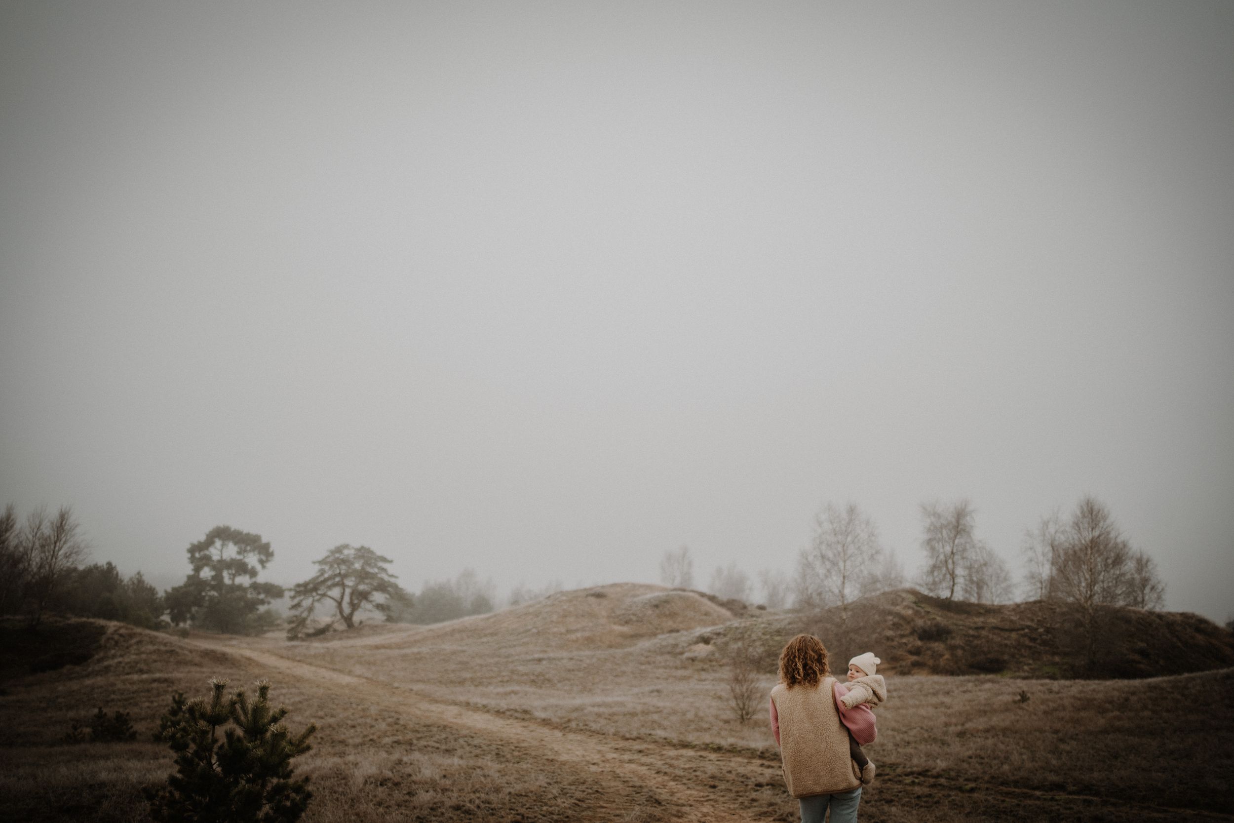 Person walking on misty hillside with dramatic foggy landscape in the background.