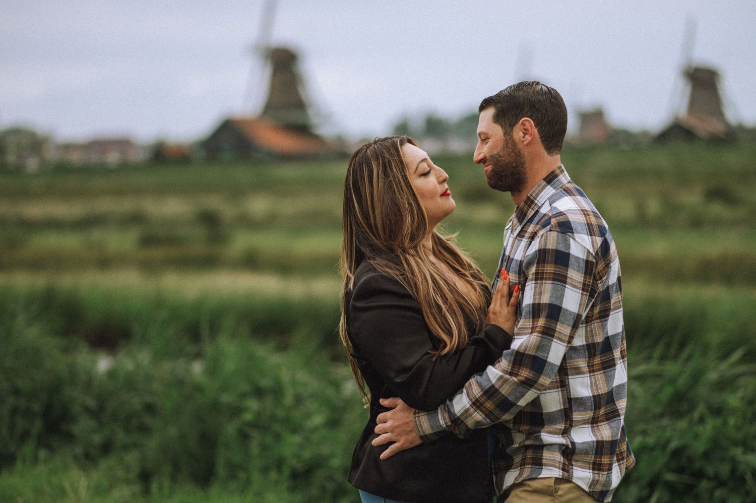 Couple embracing in outdoor field with plaid shirt and casual attire.