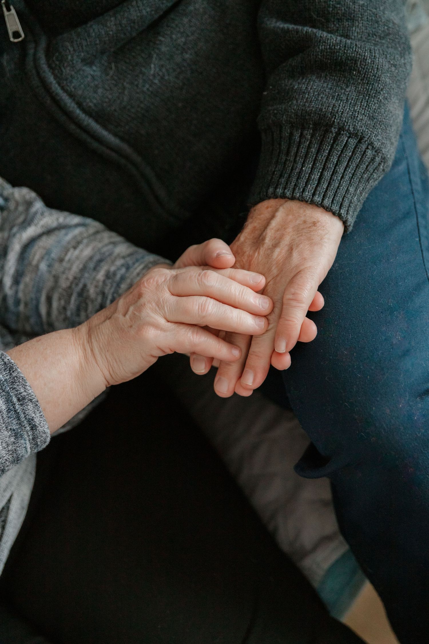 Close-up view of two hands holding each other in comfort, wearing dark and gray sweaters.