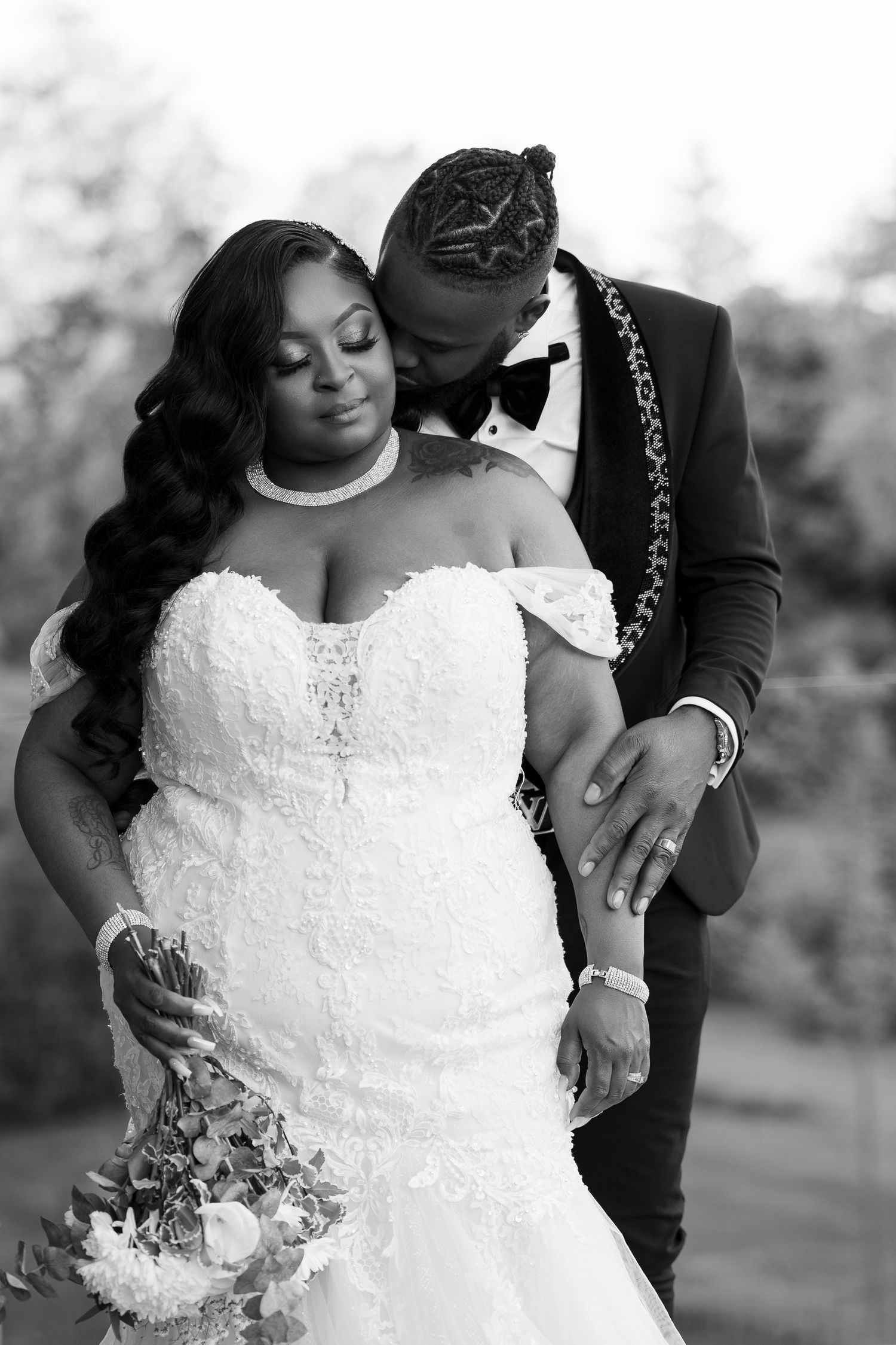 Romantic black and white wedding portrait showing tender moment between couple, with bride in lace dress and groom in tuxedo.
