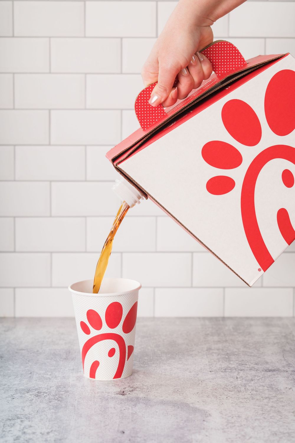 Pouring a beverage into a Chick-fil-A branded cup against white tile background.
