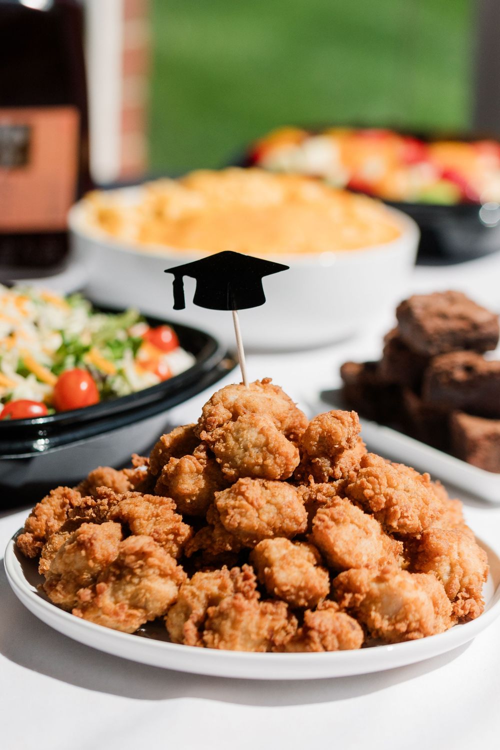 Crispy breaded chicken nuggets piled high on white plates against a green outdoor background.