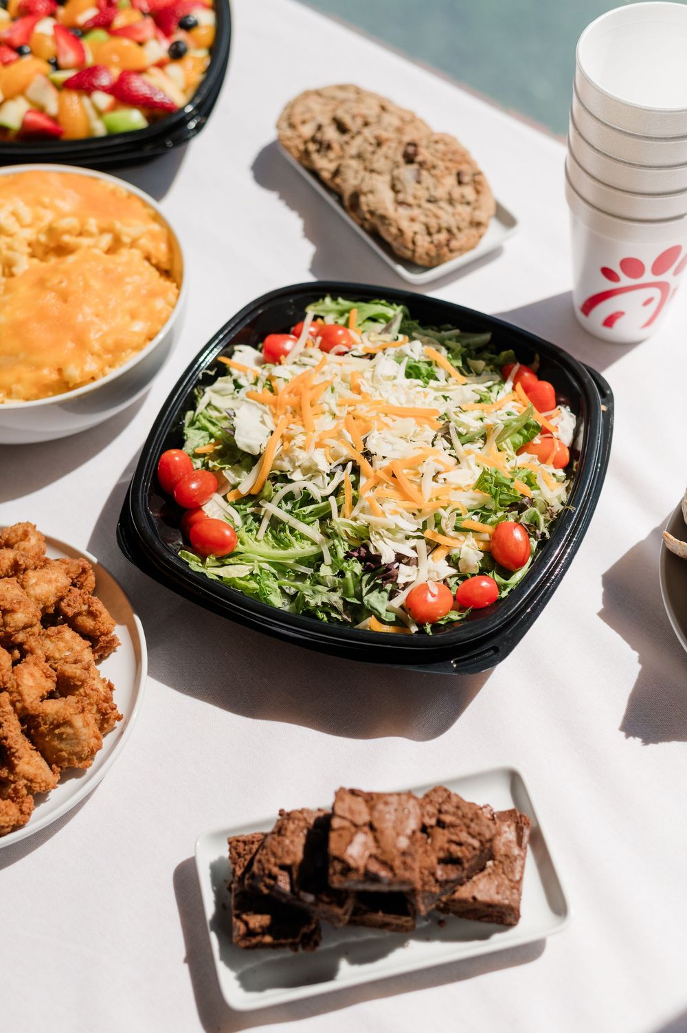 Fast food spread featuring salads, brownies, and chicken tenders arranged on white surface.