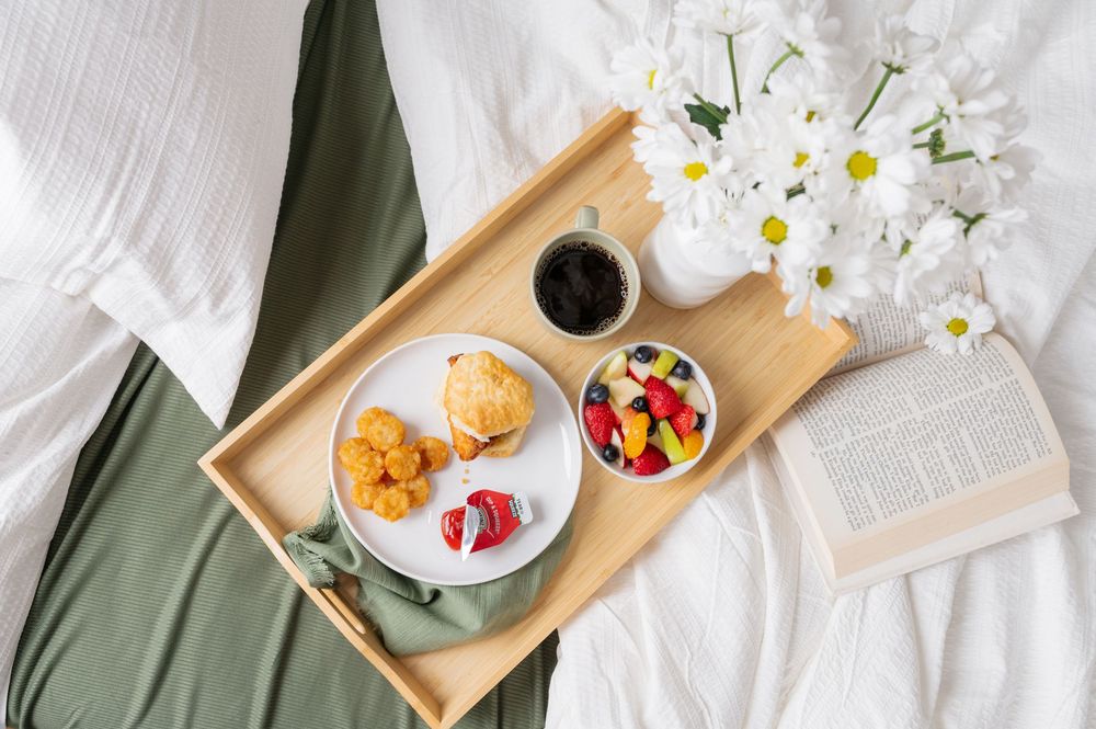 Fresh daisies in a white vase alongside a wooden serving tray with colorful snacks and beverages.