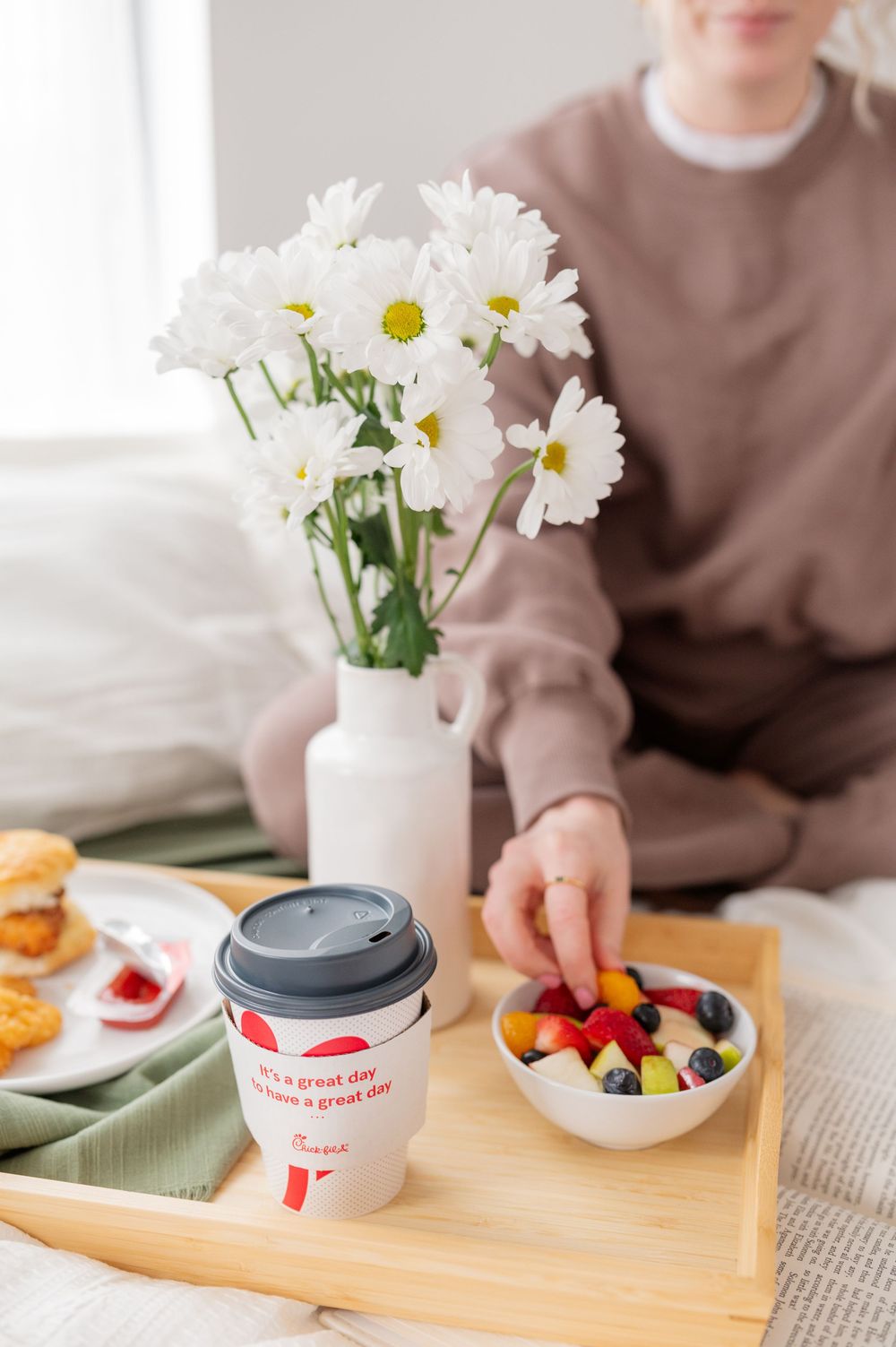 Breakfast spread on wooden tray with fresh fruit, drinks and daisies in bright morning light.