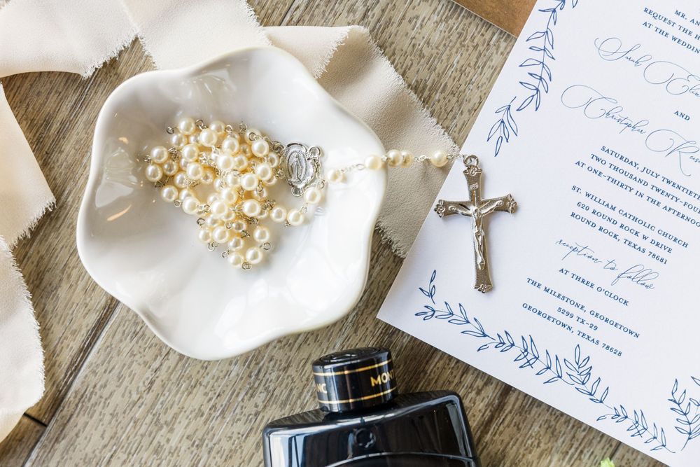 Wedding details including a pearl hair accessory, silver cross, and invitation with blue floral design.