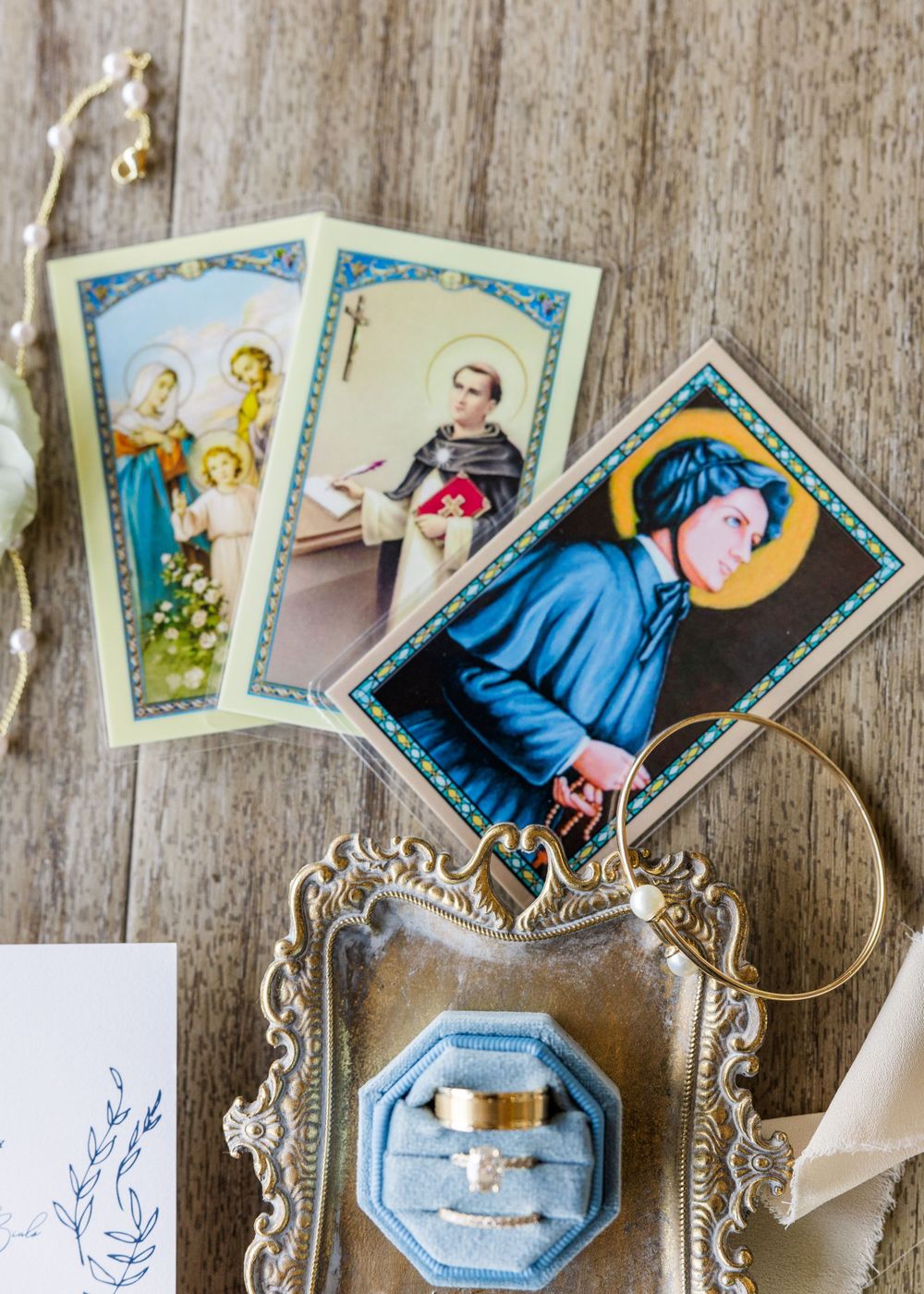 Religious prayer cards and a blue ring box arranged on rustic wooden surface.