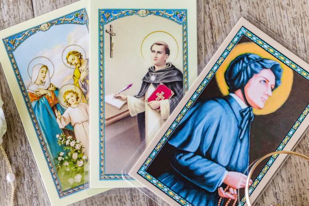 Collection of vintage religious prayer cards featuring Catholic saints and holy figures laid on wooden surface.