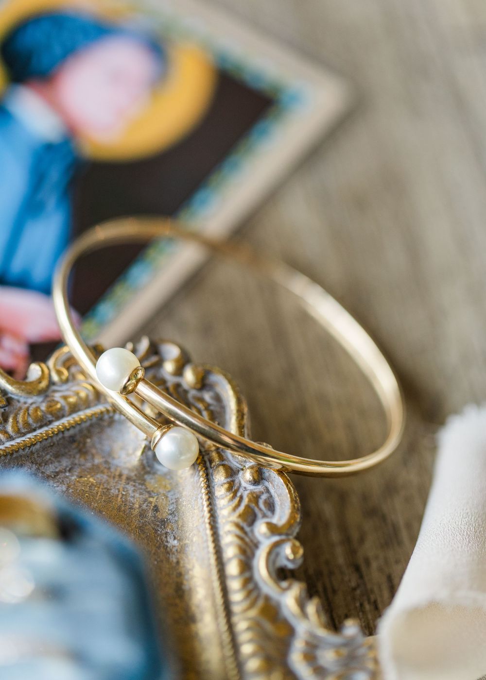A delicate gold bangle bracelet with pearl accents rests on an ornate vintage frame.