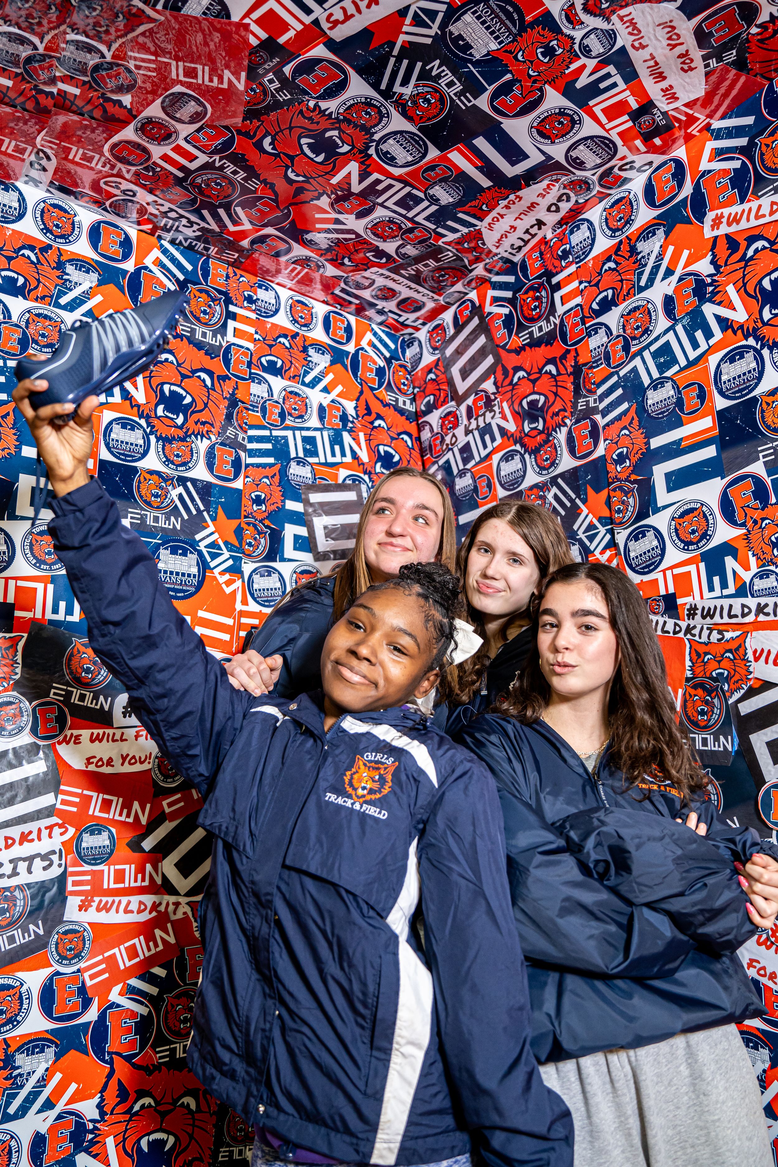 Students wearing navy blue team jackets pose together against a wall covered in orange and blue Syracuse University banners.
