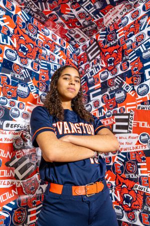 College athlete poses in navy blue varsity uniform against vibrant red and blue patterned background.