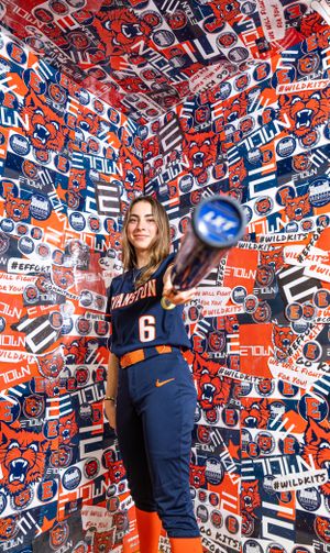 Auburn softball player poses in navy uniform against bold red and blue patterned backdrop while holding bat.