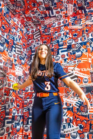 Students show school spirit against vibrant wall of blue and orange team logos and athletic designs in sports venue.