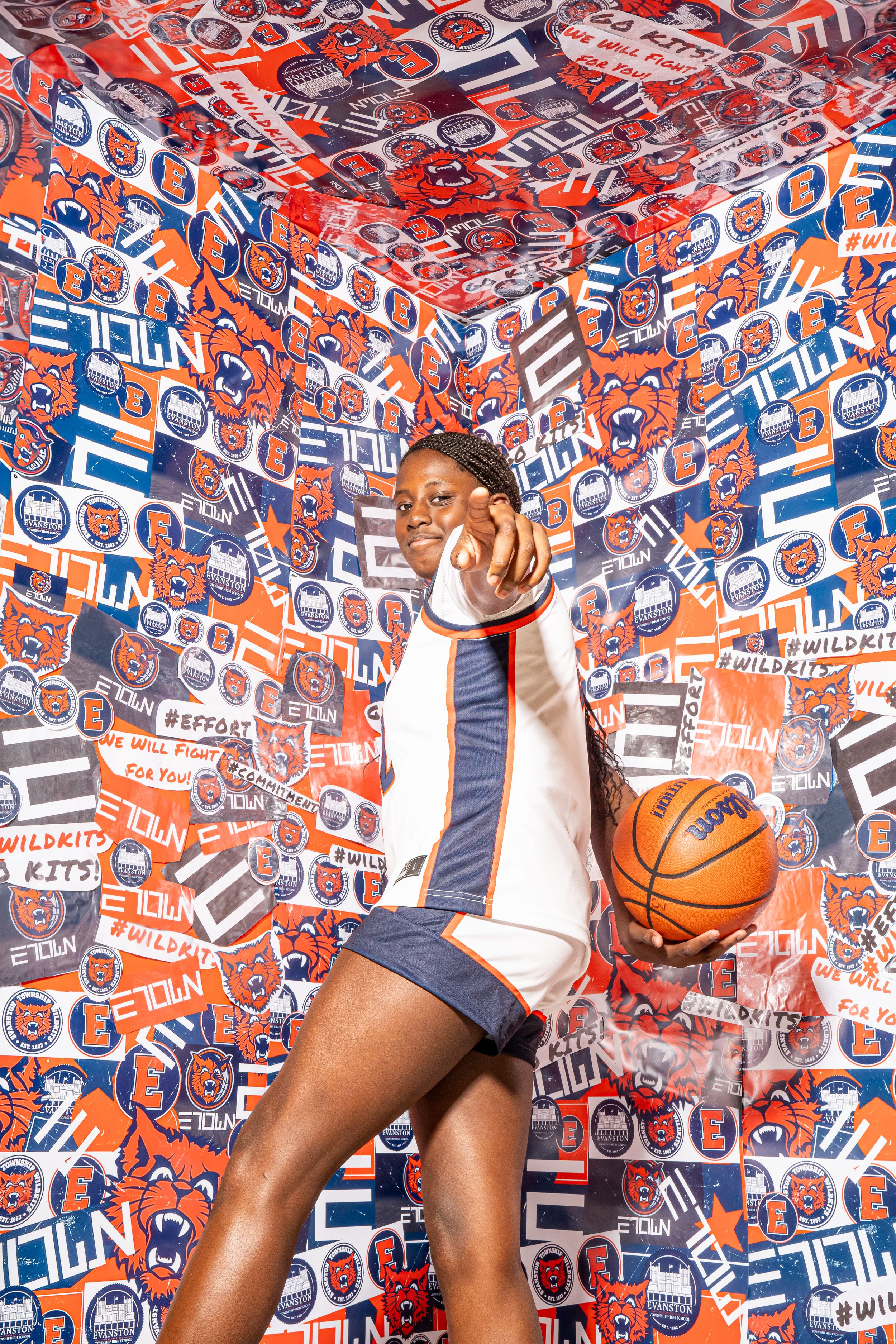 Athlete in Evanston uniform strikes playful pose against wall covered in red and blue team logos and graphics.