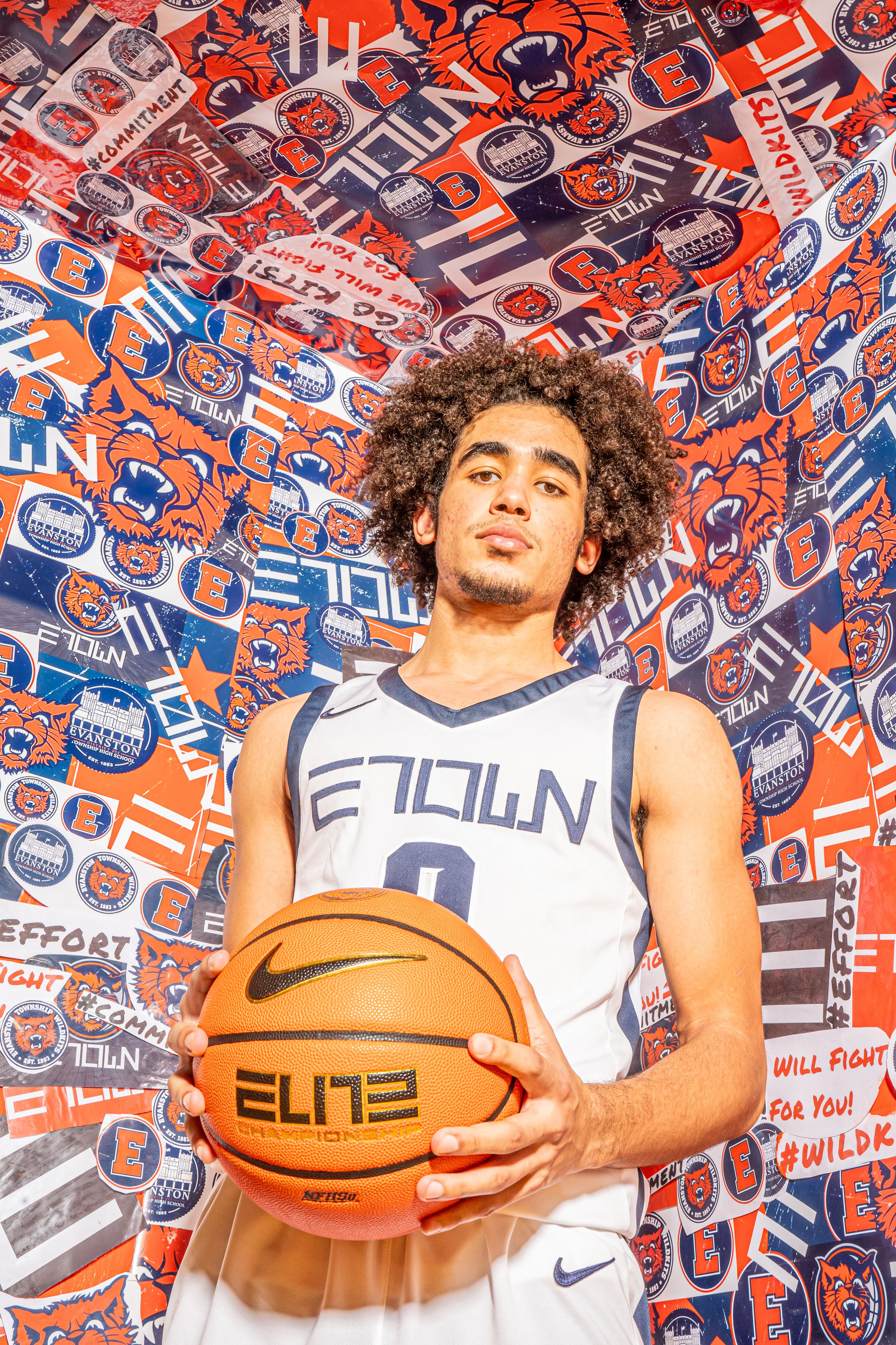 Basketball player poses with Elite basketball in front of orange and blue patterned background.