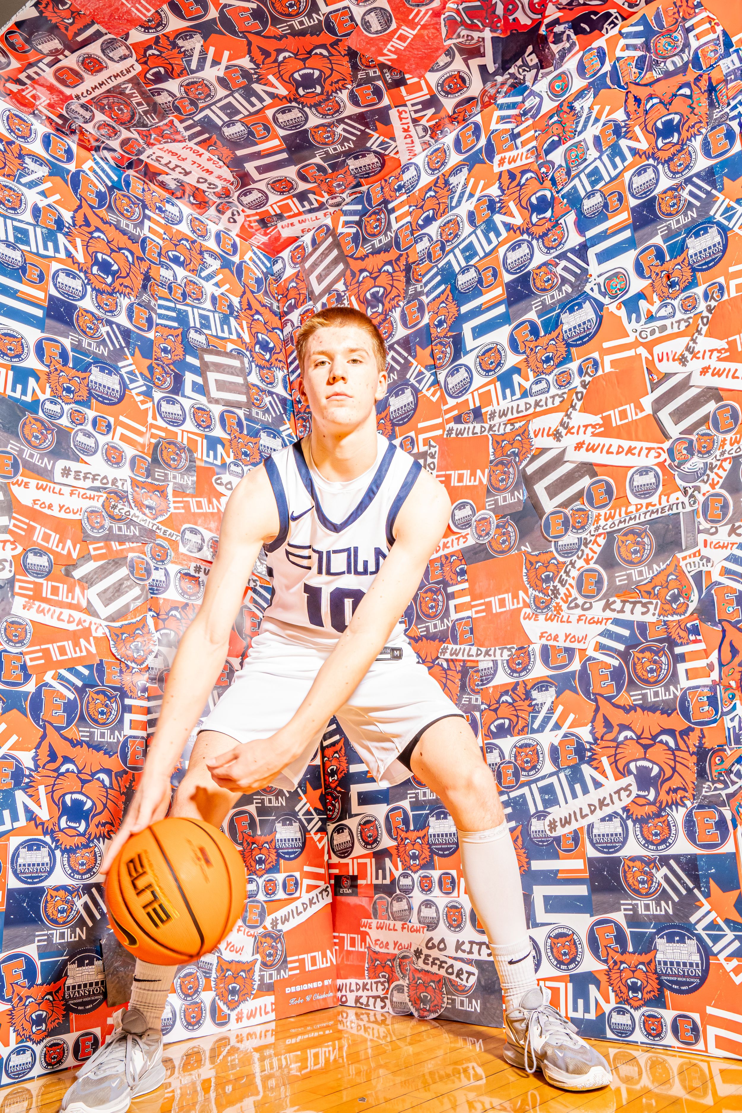 Basketball player dribbles in white uniform against wall covered in red and blue Pepsi logos.