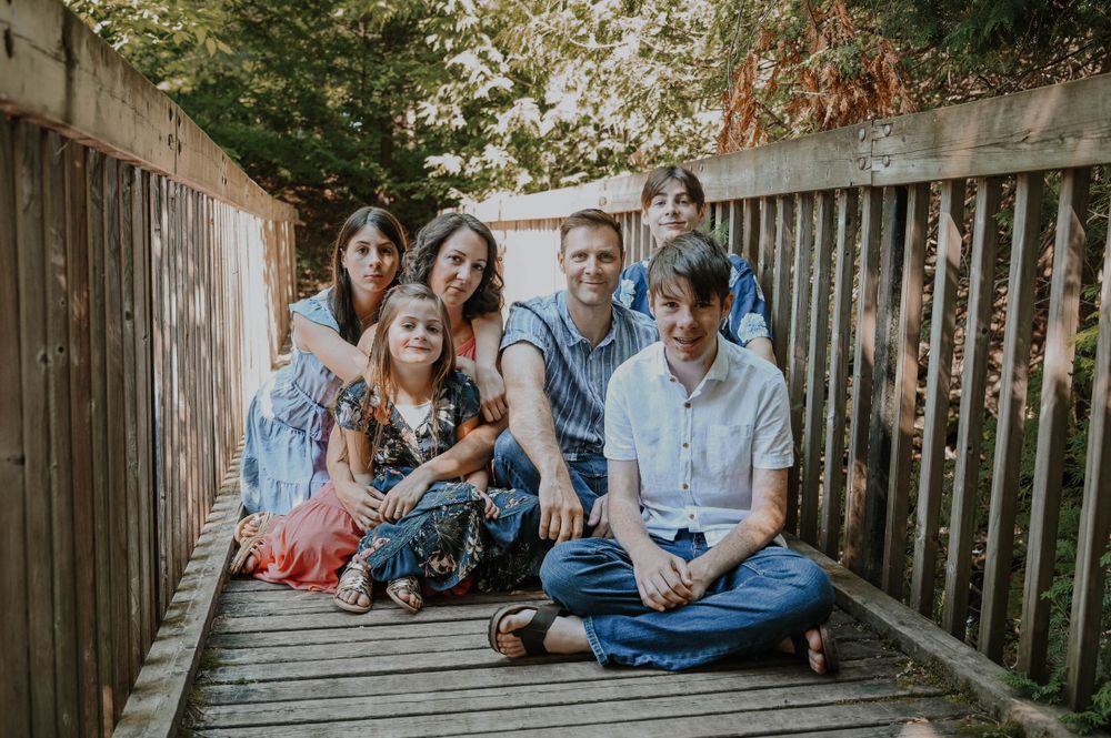 Family of five smiling together while sitting on wooden deck during autumn afternoon.
