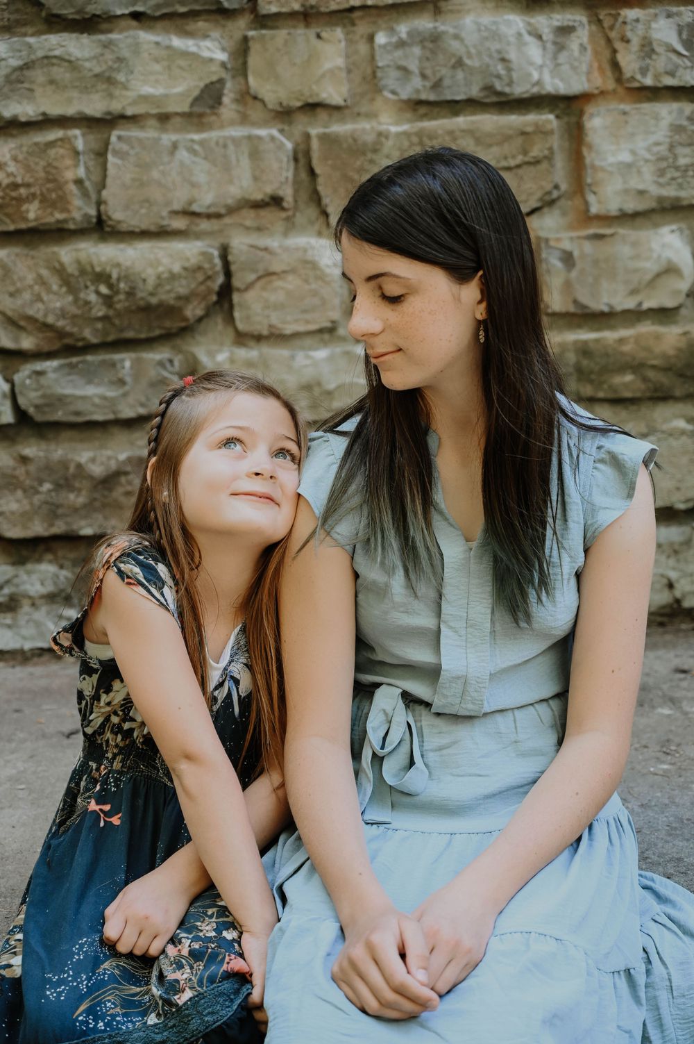 A tender moment shared between parent and child sitting together against a stone wall background in natural lighting.