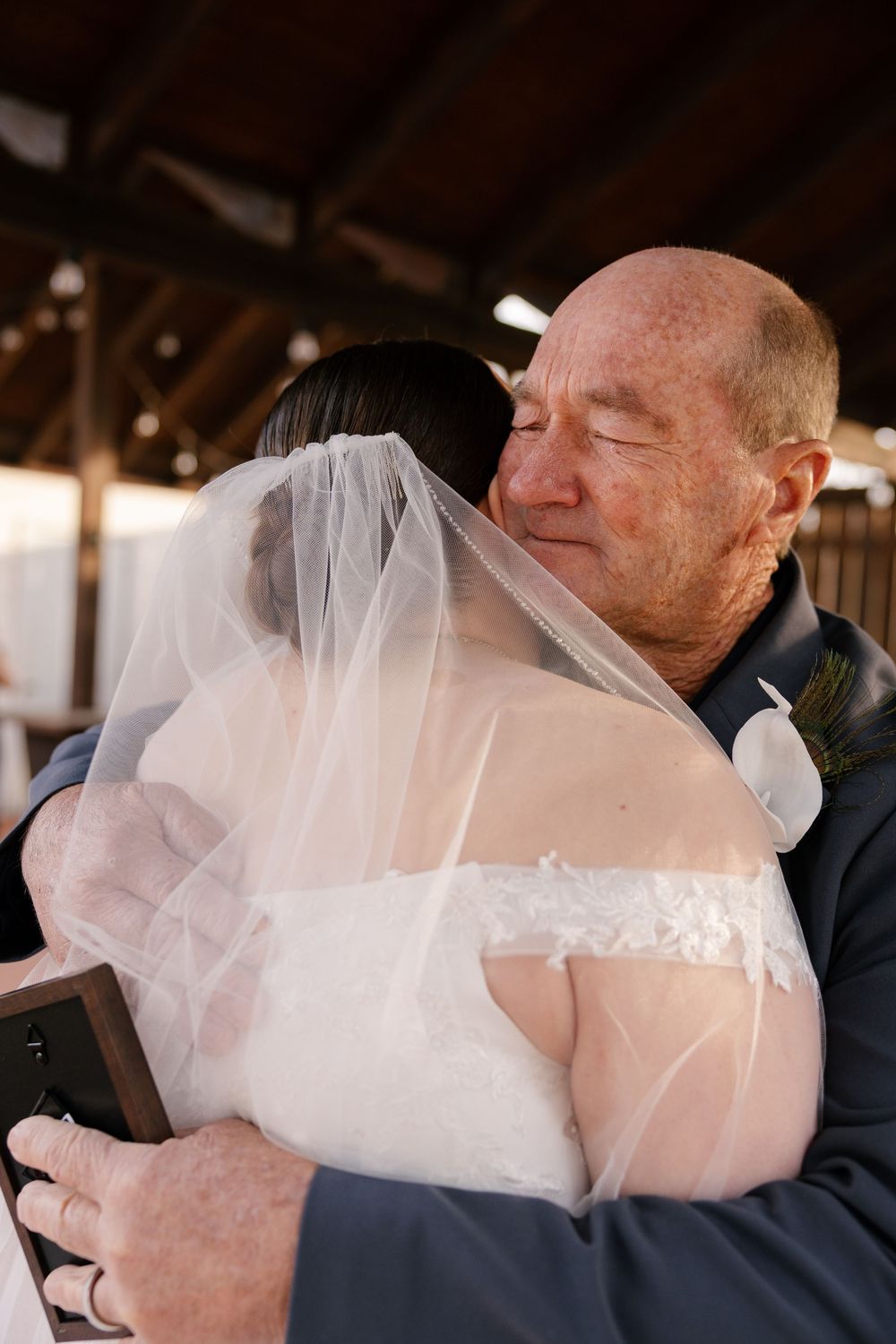 Emotional father-of-the-bride hugging his daughter in a white wedding gown and veil during wedding ceremony.