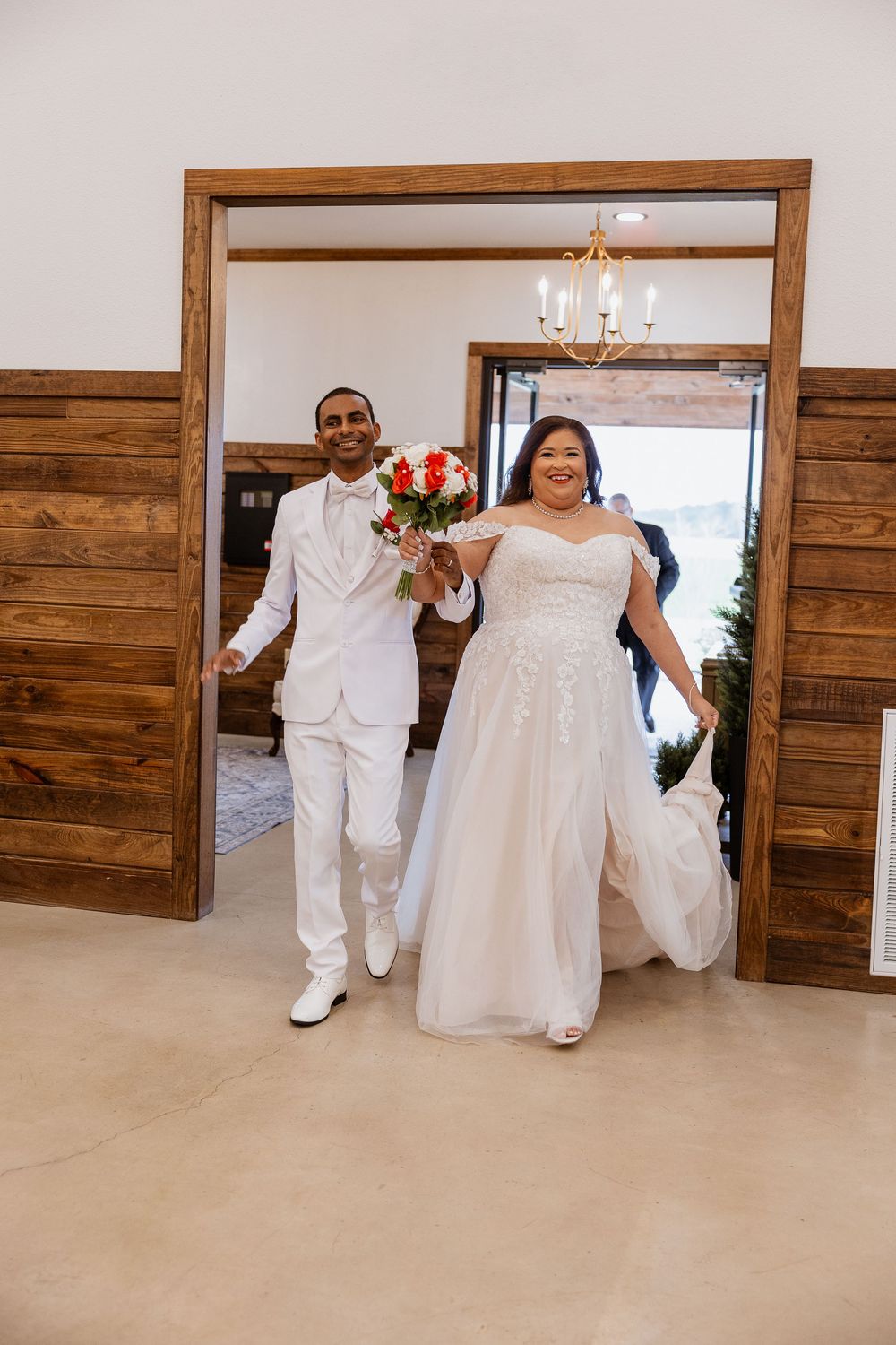 A wedding party wearing white outfits dances and celebrates in a modern venue with wooden wall panels.